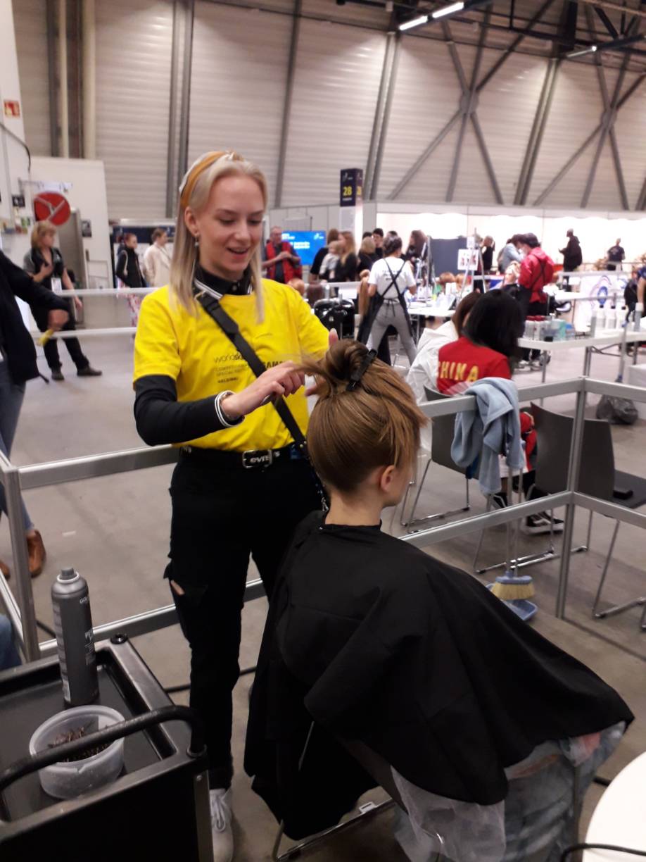 EuroSkills-kilpailija Minna Ala-Penttilä kampaamassa mallia, jolle floristiikkalajin kisaajat suunnittelivat kukka-asetelman kisatehtävään.