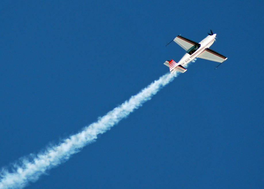 Extra-kone lentää sinisellä taivaalla. Koneen jälkeen jää valkoinen vana.