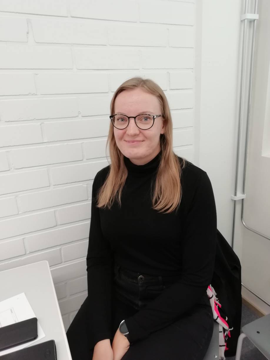 Työpaikkaohjaajaopiskelija Noora Heinonen istuu luokassa muistiinpanovälineet edessään pöydällä.