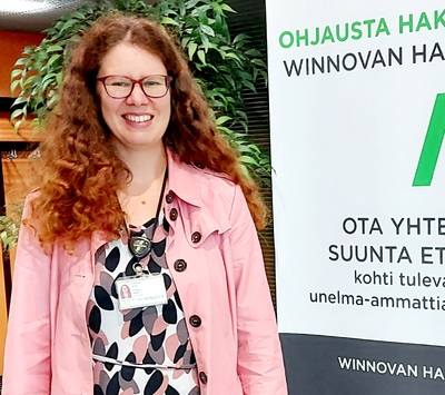 Niina Engblom hymyilevänä WinNovan mainosstandin vieressä.