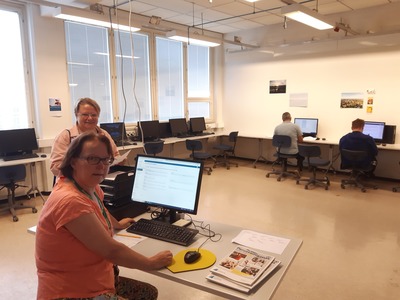 Kuvassa pöydän ääressä Irja Tauriainen sekä takana S2-opettaja Mirjam Voutilainen. Taustalla opiskelijoita tietokoneilla Rauman uusissa YTO-osaamon tiloissa.