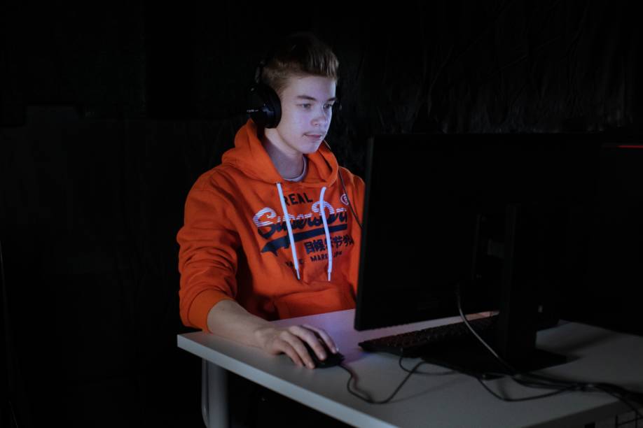 Oranssipaitainen Miro Nummela pelaamassa tietokoneella.
