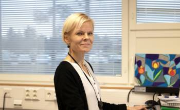 Vaaleahiuksinen nainen musta-valkoisessa paidassa katsoo kameraan.