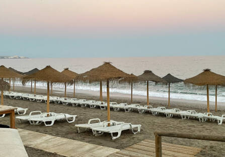 Pastellisävyinen aamu Fuengirolan rannalla. Kuvassa meri, aurinkotuoleja ja aurinkovarjoja.