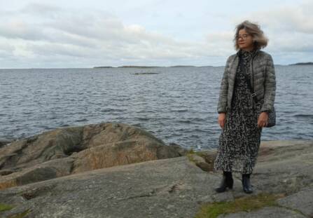 Harmahtavahiuksinen nainen seisoo meren rannalla.