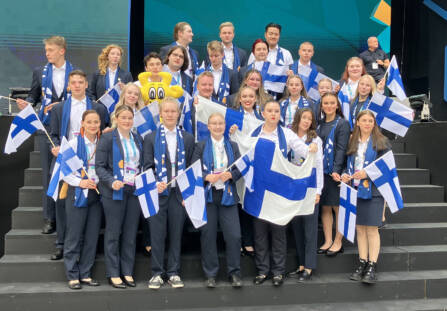 Suomen kilpailujoukkue poseeraa Suomen liput käsissään EuroSkills kilpailussa.