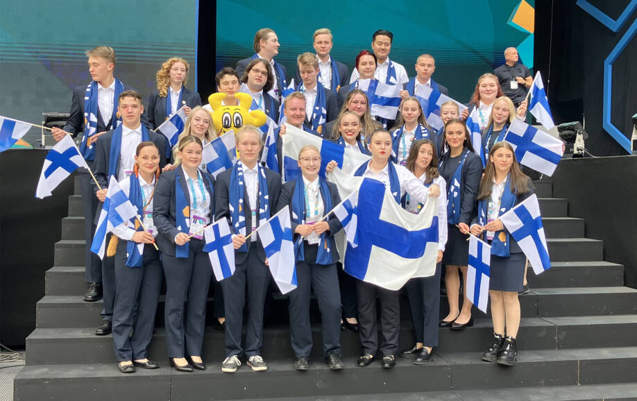 Suomen kilpailujoukkue poseeraa Suomen liput käsissään EuroSkills kilpailussa.