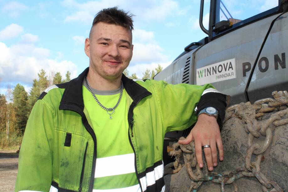 Hymyilevä, lyhythiuksinen nuori mies nojaa metsäkoneen renkaaseen. Hänellä on paksu kaulaketju kaulassa. Vasemmassa kädessä on kello ja sormus keskisormessa. Miehellä on päällään huomiokeltaiset työvaatteet.