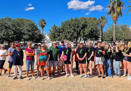 Paljon väkeä ryhmäkuvassa aurinkoisella hiekkarannalla ulkomailla. Taivas on kirkkaansininen. Kuvassa oikealla olevilla henkilöillä on WinNovan t-paidat päällään.