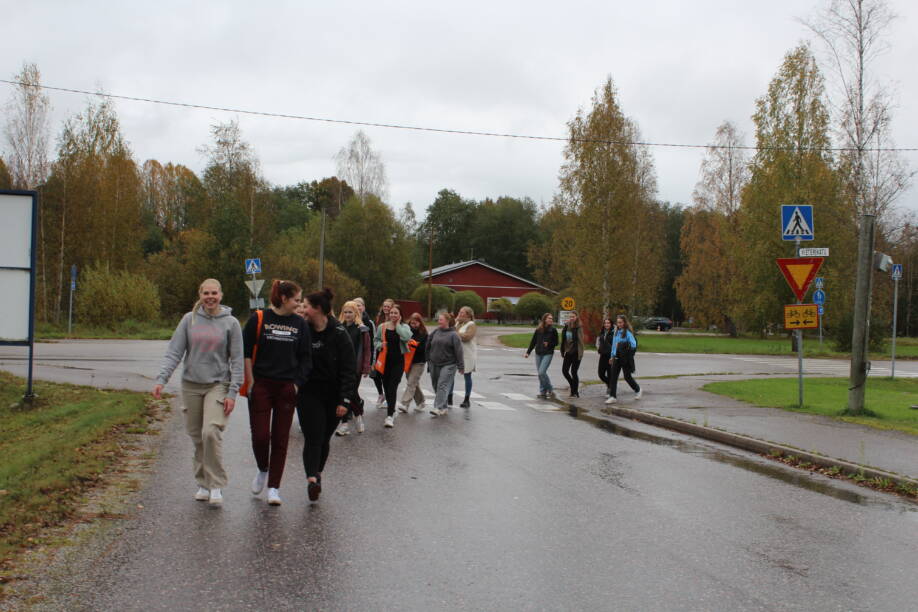 Opiskelijat kävelevät sateisella tiellä.