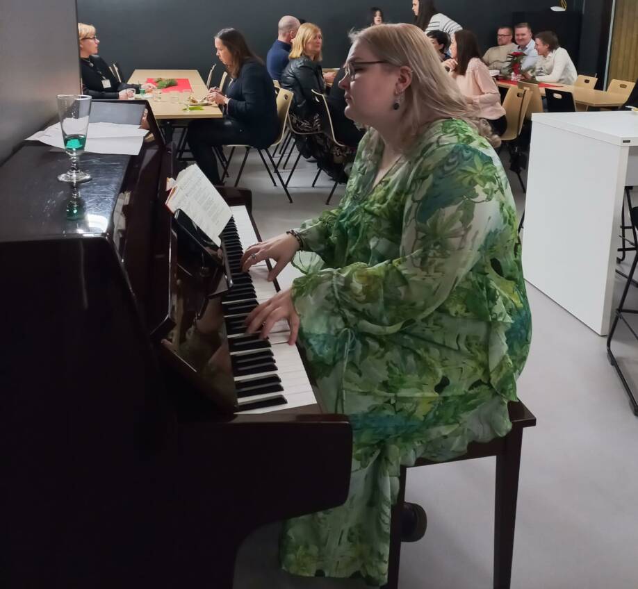 Vihreämekkoinen nainen soittaa pianoa.
