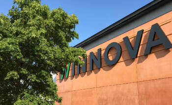 Kesäinen kuva, vaahtera oranssin seinän edessä sinistä taivasta vasten. Seinässä iso WINNOVA-logo.