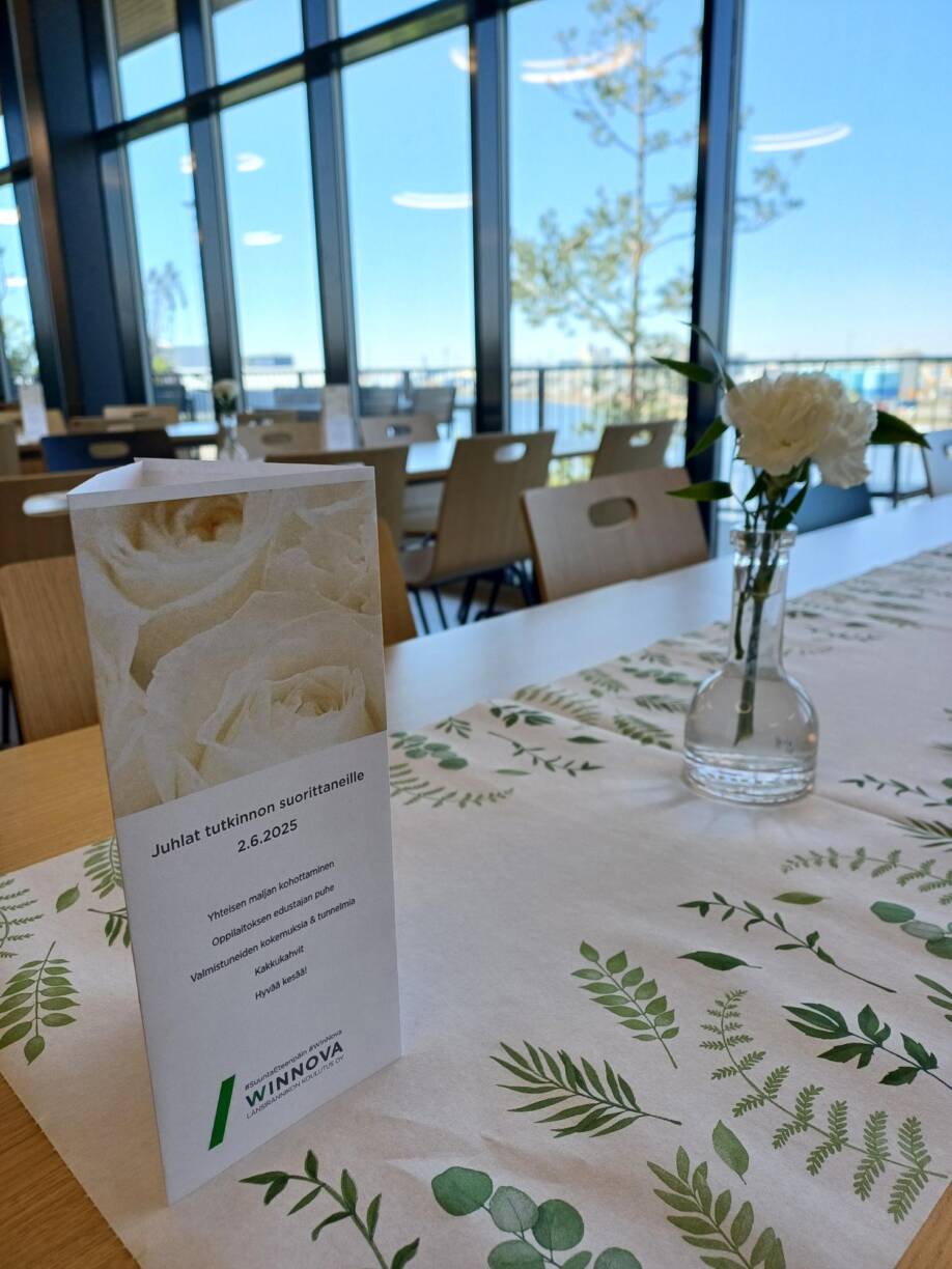 WinNovan juhlat Raumalla. Ohjelma ja kukka pöydällä.