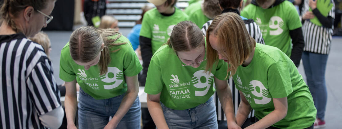 Taitaja9-kilpailua. Yläkoululaiset tehtävän ääressä ja tuomari valvoo.