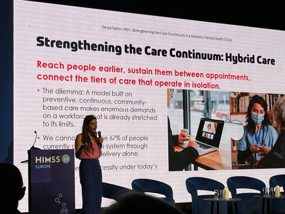 Derya Sahin esittelee esiintymislavalla hoitoratkaisuja. Taustalla suuri valkokangas, jossa tietoja ratkaisuista.